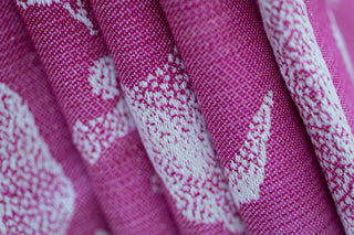 Close-up of pink fabric with white dinosaurs - folded to show details of weave and sparkle threads - Jurassic Park Princess preorder woven wrap fabric, available for a limited time at Mama & Roo's