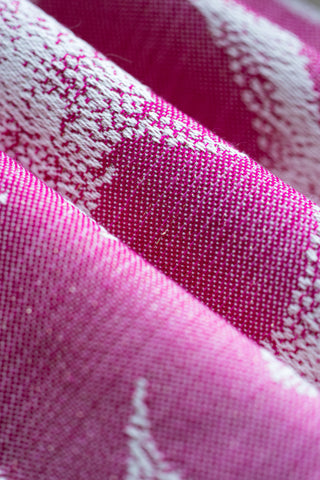 Close-up of pink fabric with white dinosaurs - folded to show details of weave - Jurassic Park Princess preorder woven wrap fabric, available for a limited time at Mama & Roo's