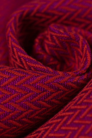 Closeup of swirled babywearing wrap fabric in cotton woven design Sedona, a beautiful rich red with hints of orange in a herringbone weave