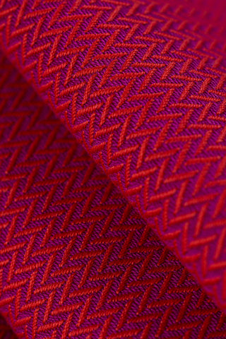 Closeup of folded babywearing wrap fabric in cotton woven design Sedona, a beautiful rich red with hints of orange in a herringbone weave