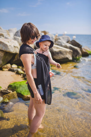 Model wears toddler in black water ring sling lakeside