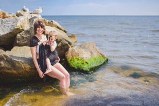 Model wears toddler in black water ring sling lakeside