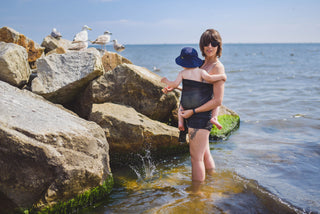 Model wears toddler in black water ring sling lakeside